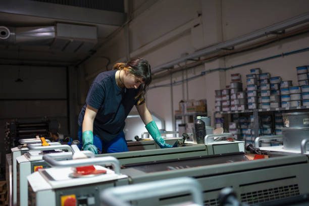 Technician inspecting and cleaning offset printing rollers to reduce color variation during print runs.