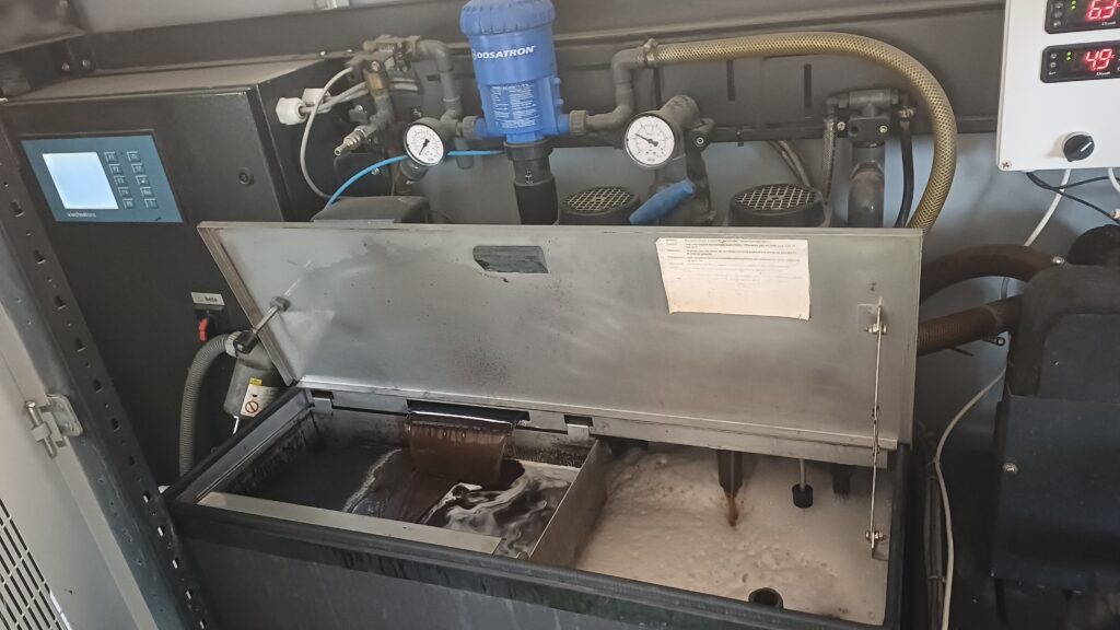 High-resolution photograph of a Technotrans Beta industrial central dampening solution preparation unit, featuring a Dosatron proportional doser and an open tank showing a clear separation between the dark liquid solution and rich foam.
