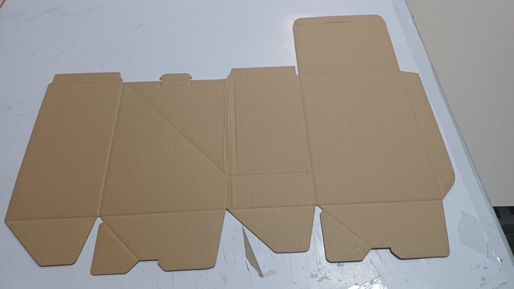 Flat die-cut corrugated cardboard box blank displaying precise crease lines and cut flaps for assembly.