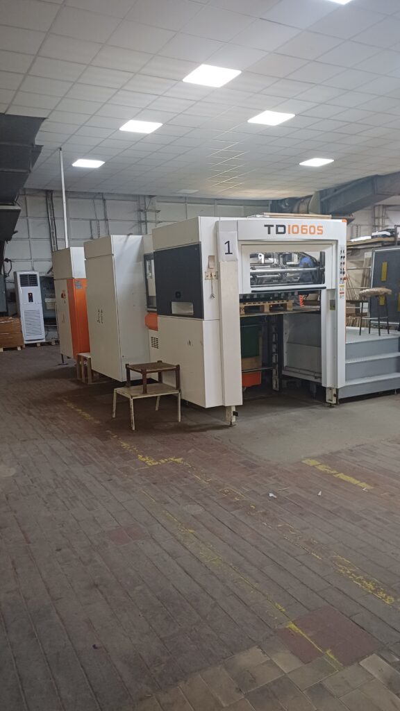 Industrial automatic flatbed die cutting machine TD1060S in a postpress production facility.